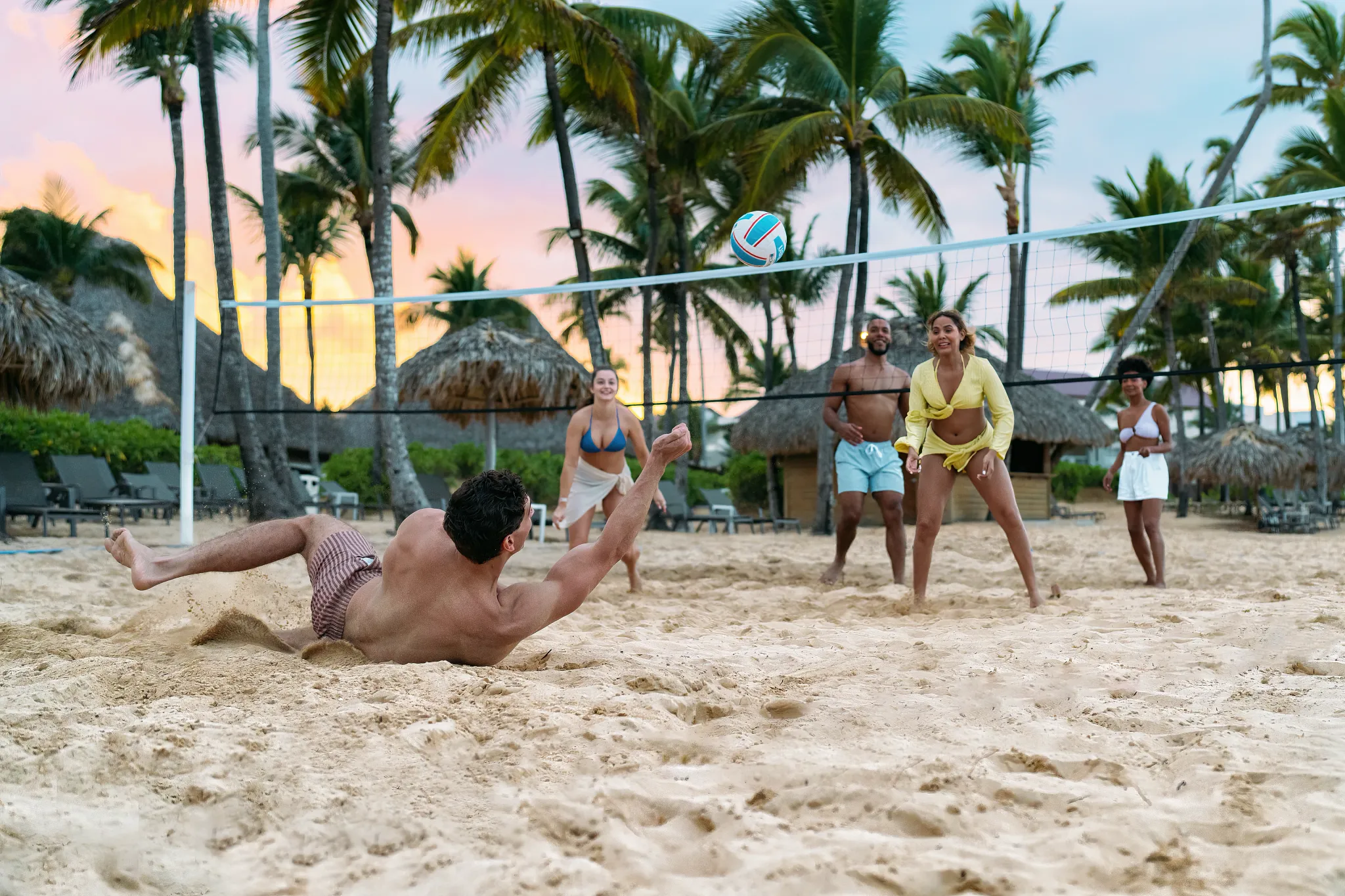 Guests playing beach volleyball at Breathless Punta Cana with palm trees and sunset skies in the background.