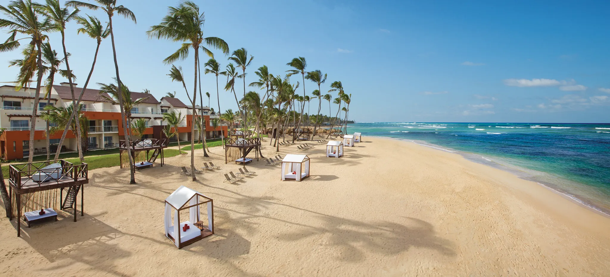 Panoramic beach view at Breathless Punta Cana with palm trees, cabanas, and turquoise ocean.